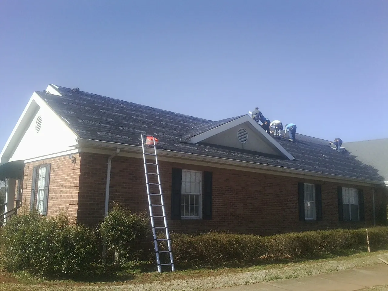 Crew tearing shingles off a brick ranch roof with a ladder set — Metal Roof Repair work by our crew in Citrus Heights