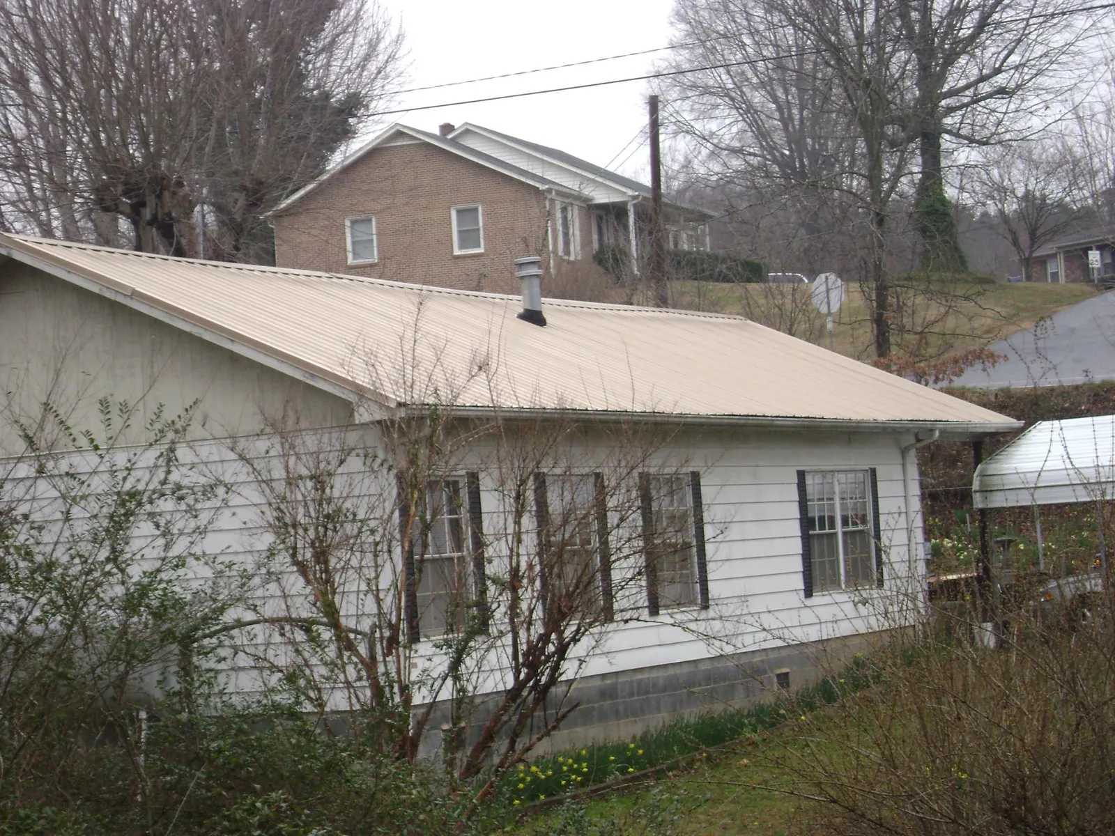 Tan metal roof on a white sided house set into a hillside — Commercial Roofing by Roofing Brothers in Citrus Heights